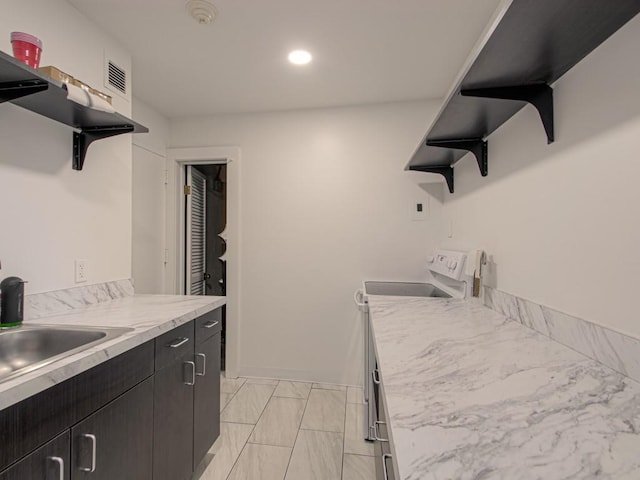 kitchen featuring open shelves, electric range oven, dark cabinetry, light marble finish floors, and light countertops