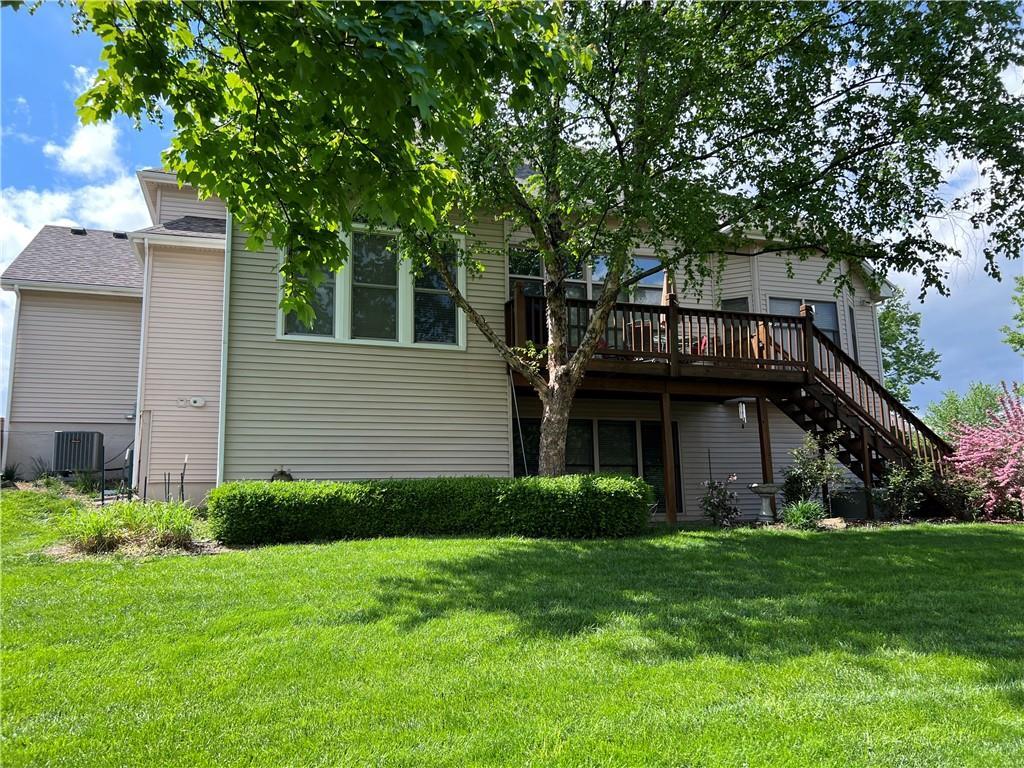 rear view of property featuring a yard, a deck, cooling unit, and stairs