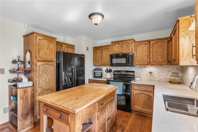 kitchen with black appliances, a sink, wood finished floors, and butcher block counters