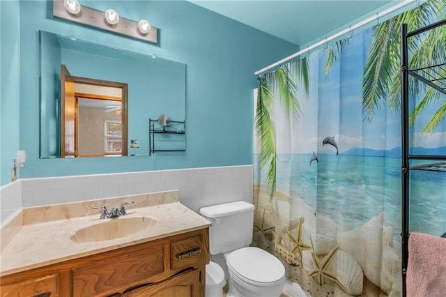 bathroom with toilet, a shower with curtain, vanity, tile walls, and a wainscoted wall