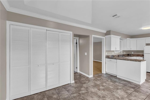 kitchen featuring visible vents, freestanding refrigerator, crown molding, dark countertops, and a sink