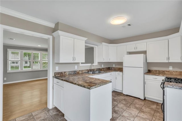 kitchen with a sink, freestanding refrigerator, a peninsula, and white cabinetry
