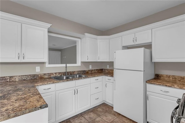kitchen featuring a sink, dark countertops, white cabinets, and freestanding refrigerator
