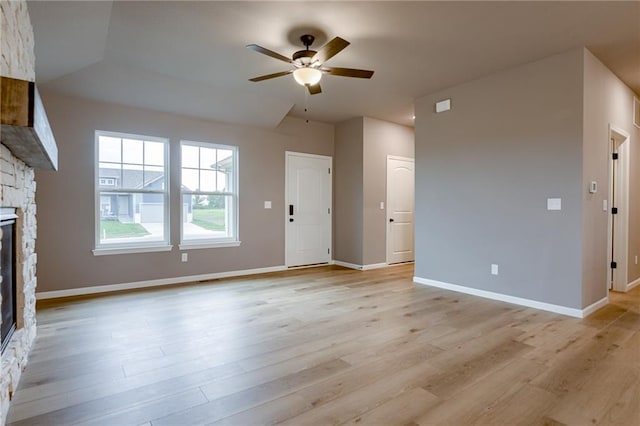 unfurnished living room with a stone fireplace, baseboards, ceiling fan, and light wood-type flooring