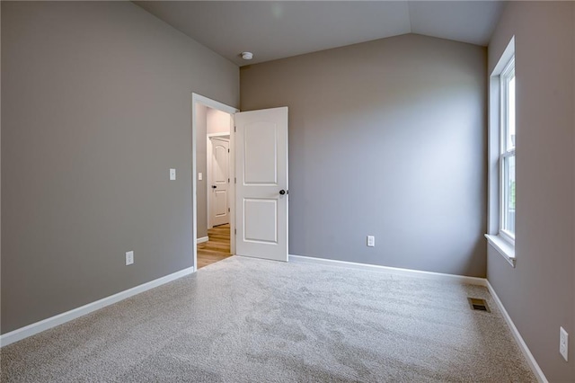 carpeted spare room with baseboards, visible vents, a wealth of natural light, and lofted ceiling