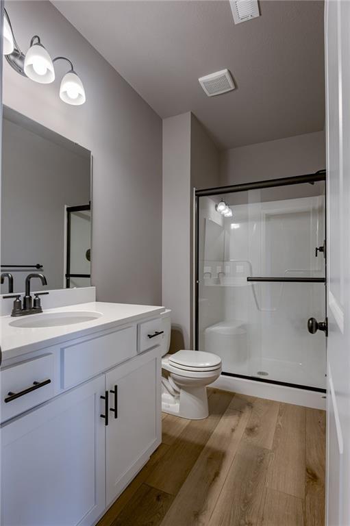 bathroom featuring toilet, visible vents, a shower stall, and wood finished floors