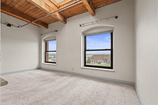 carpeted empty room featuring baseboards, arched walkways, beam ceiling, and wood ceiling