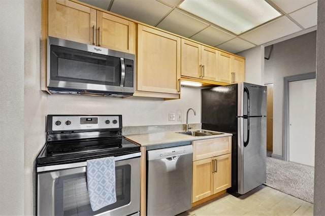 kitchen featuring light brown cabinetry, appliances with stainless steel finishes, a sink, light countertops, and a paneled ceiling