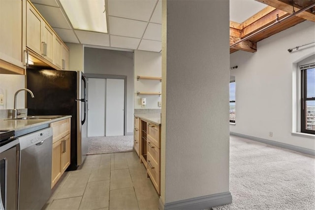 kitchen with stainless steel dishwasher, light brown cabinetry, light carpet, a paneled ceiling, and a sink