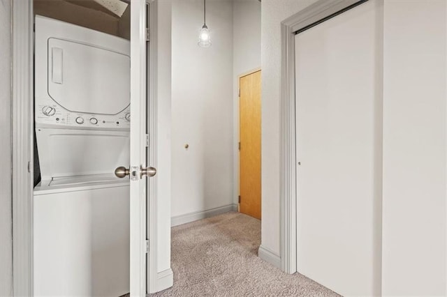 corridor with carpet floors, baseboards, and stacked washing maching and dryer
