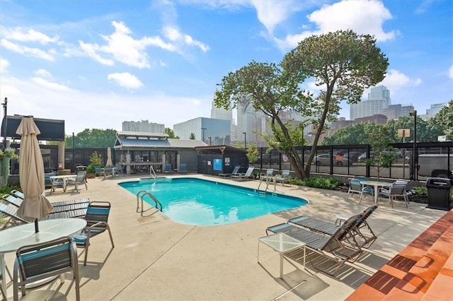 community pool with a view of city, fence, outdoor dining area, and a patio area