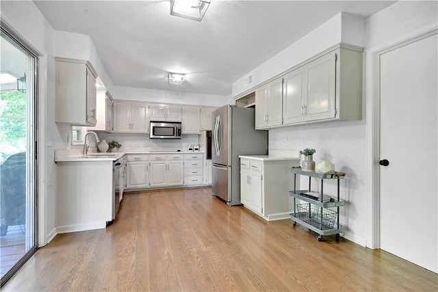 kitchen with stainless steel appliances, a sink, light countertops, and wood finished floors