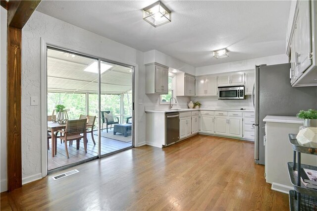 kitchen with appliances with stainless steel finishes, light countertops, light wood-style floors, a textured wall, and a sink