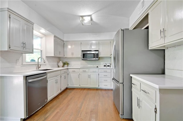 kitchen with appliances with stainless steel finishes, a sink, light countertops, light wood-style floors, and tasteful backsplash