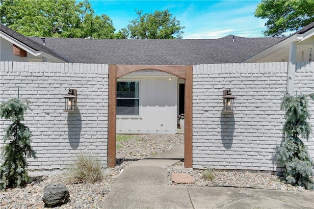 view of exterior entry with a shingled roof, board and batten siding, and brick siding