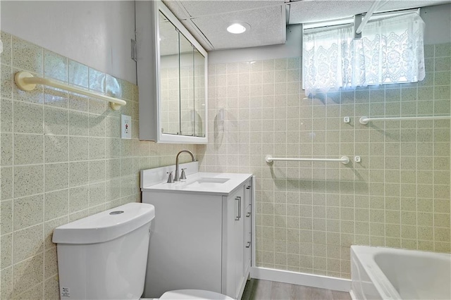 full bathroom with toilet, a tub, tile walls, and vanity