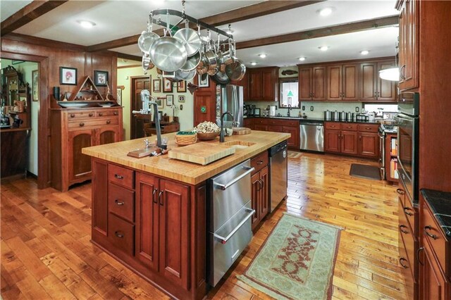 12 Woodland Trl, Warrensburg, MO 64093 - kitchen with appliances with stainless steel finishes, light wood-style flooring, an island with sink, beamed ceiling, and a sink