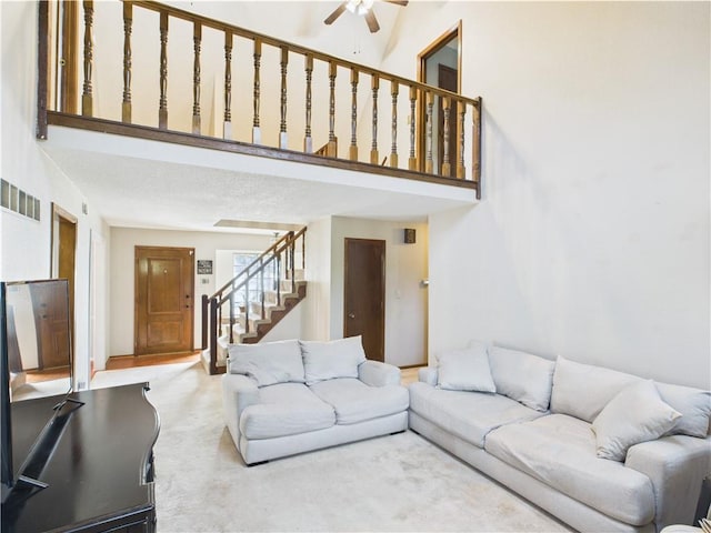 carpeted living area with stairs, ceiling fan, and a towering ceiling