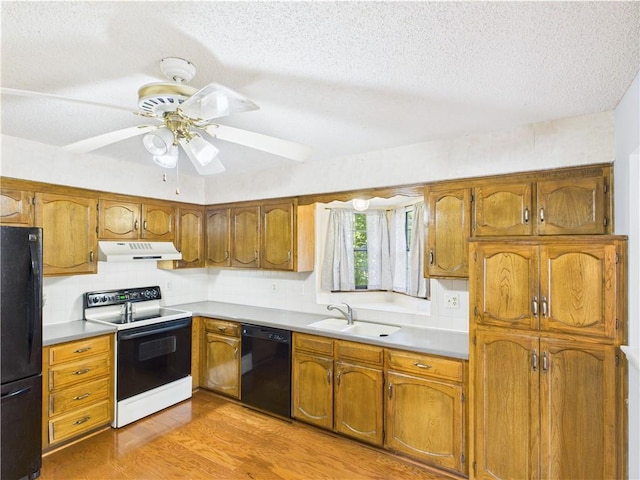 kitchen featuring black appliances, under cabinet range hood, a sink, a textured ceiling, and light wood-style flooring