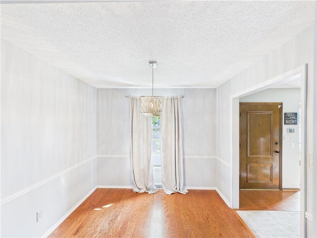 unfurnished dining area featuring wood finished floors, a textured ceiling, a chandelier, and baseboards