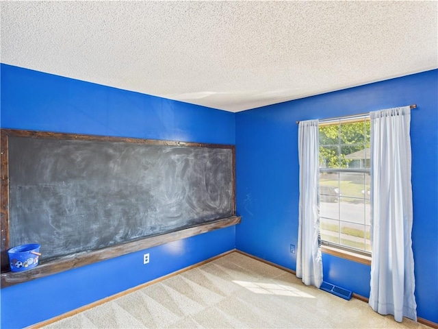 spare room with a textured ceiling, carpet flooring, and baseboards