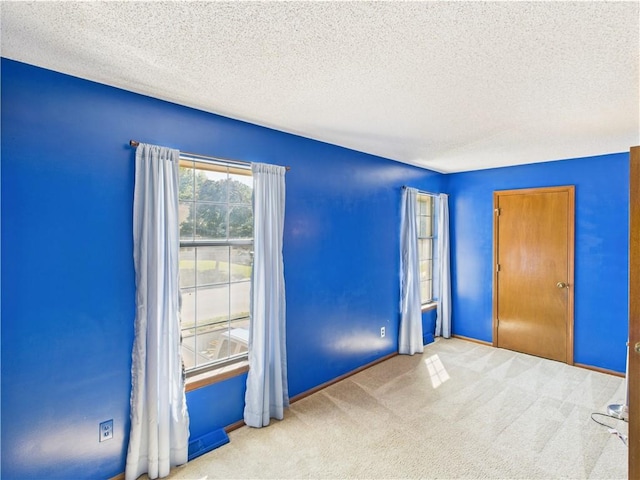 carpeted empty room featuring a textured ceiling and baseboards