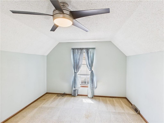 additional living space featuring a textured ceiling, vaulted ceiling, ceiling fan, carpet floors, and baseboards