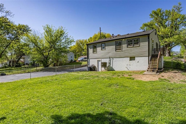 rear view of property featuring a yard, driveway, stairway, and fence
