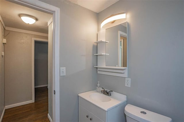 bathroom featuring toilet, wood finished floors, crown molding, baseboards, and vanity