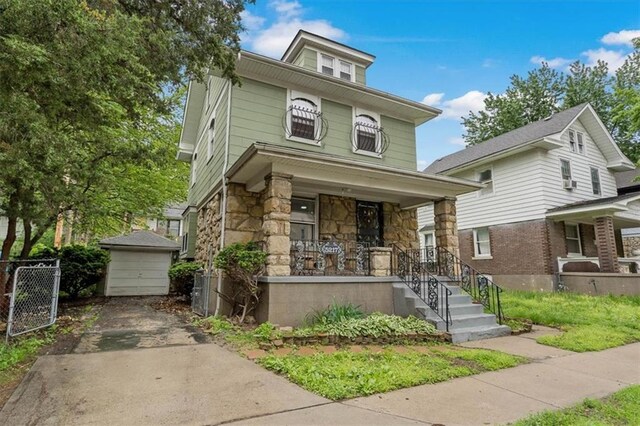 american foursquare style home with covered porch, stone siding, fence, driveway, and an outdoor structure