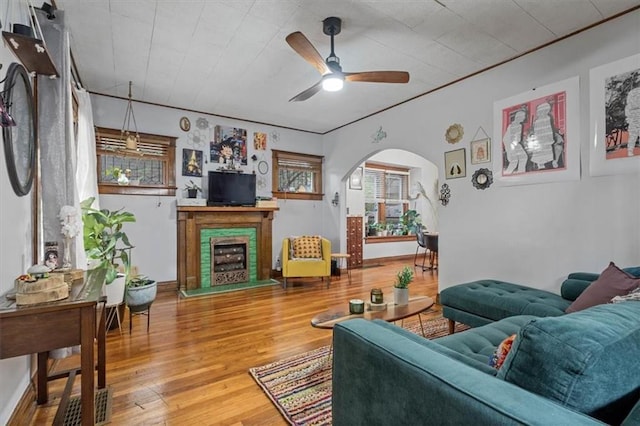 living room with a ceiling fan, arched walkways, wood finished floors, and a fireplace