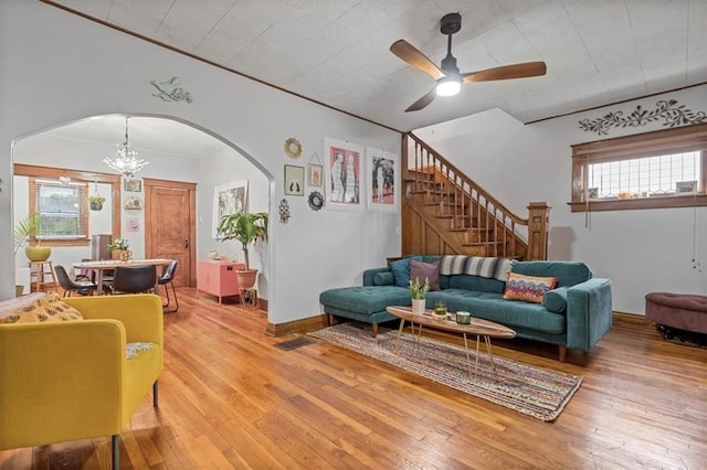 living room with arched walkways, light wood-style floors, stairs, and ceiling fan