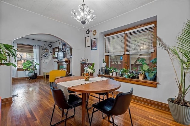 dining area featuring arched walkways, a chandelier, hardwood / wood-style floors, and baseboards