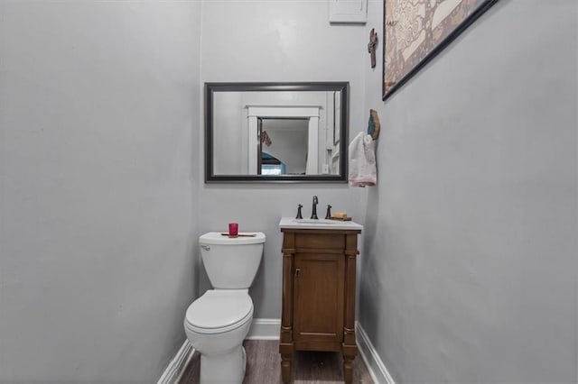 bathroom with toilet, wood finished floors, baseboards, and vanity