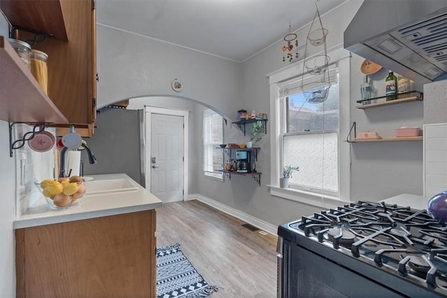 kitchen with open shelves, arched walkways, ventilation hood, black gas range oven, and a sink