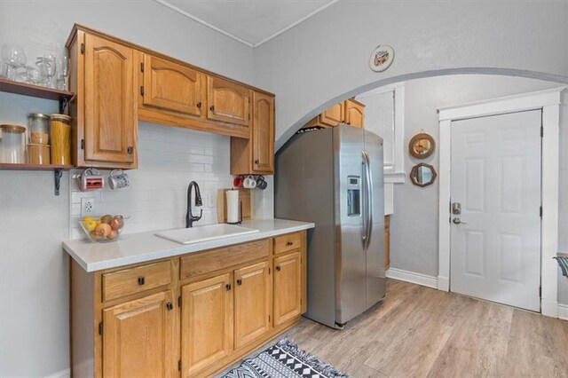 kitchen featuring a sink, stainless steel fridge with ice dispenser, arched walkways, light countertops, and tasteful backsplash
