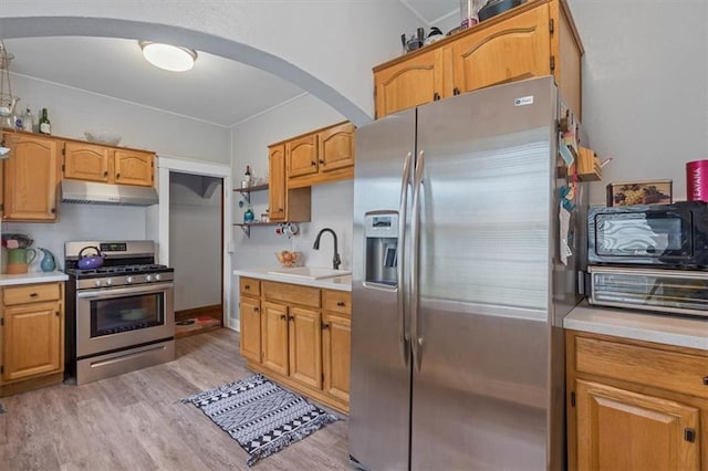 kitchen with appliances with stainless steel finishes, a sink, under cabinet range hood, arched walkways, and light wood finished floors