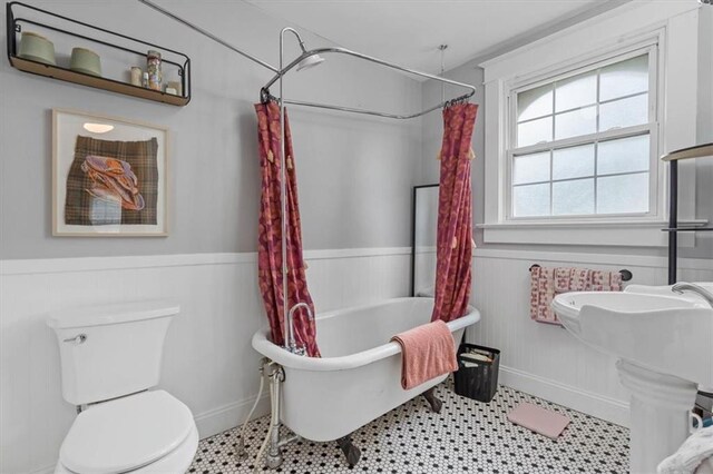 full bath with a wainscoted wall, a bath, toilet, baseboards, and curtained shower