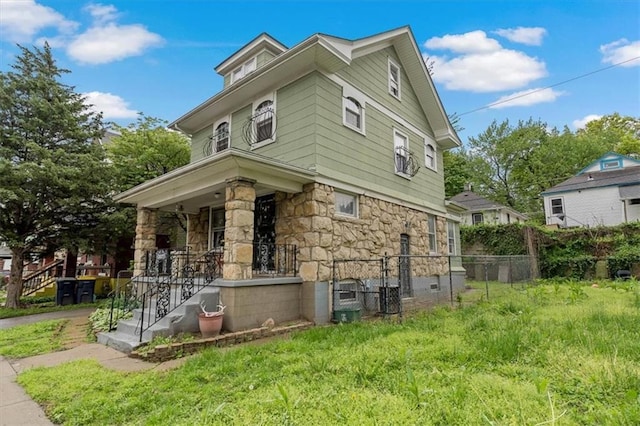 view of front of property with stone siding, a porch, and fence