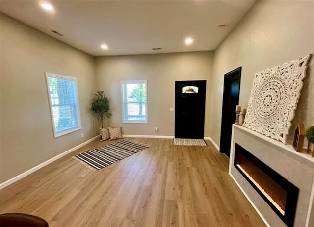 foyer entrance featuring healthy amount of natural light, wood finished floors, baseboards, a glass covered fireplace, and recessed lighting