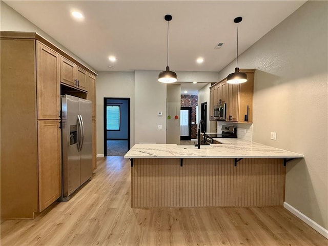 kitchen with appliances with stainless steel finishes, light wood finished floors, a peninsula, light stone countertops, and recessed lighting