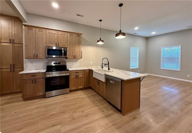 kitchen featuring stainless steel appliances, a sink, a peninsula, light wood finished floors, and recessed lighting