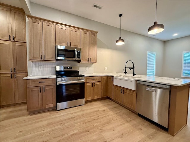 kitchen with appliances with stainless steel finishes, a sink, a peninsula, and light wood-style floors