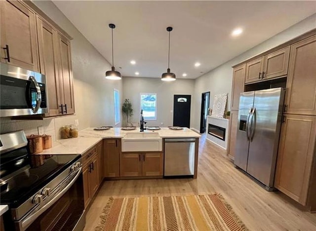 kitchen with stainless steel appliances, a sink, light wood-style flooring, a peninsula, and a glass covered fireplace