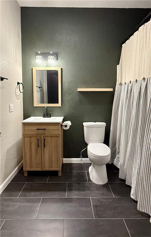 bathroom featuring vanity, toilet, baseboards, a textured wall, and tile patterned flooring