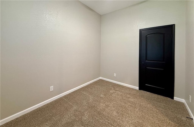 unfurnished room featuring dark colored carpet and baseboards
