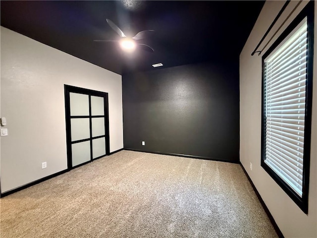 carpeted spare room featuring a ceiling fan and baseboards