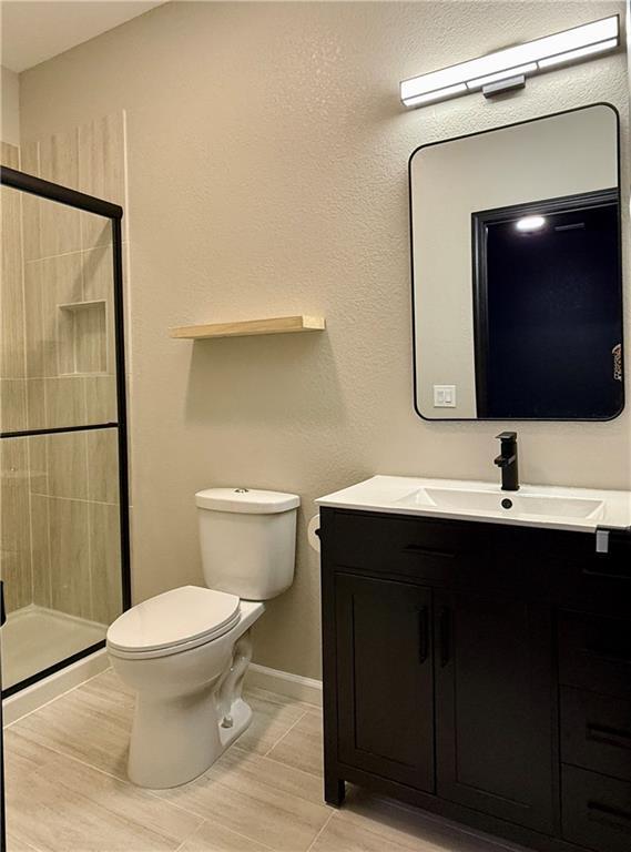 full bathroom featuring a stall shower, toilet, vanity, and baseboards