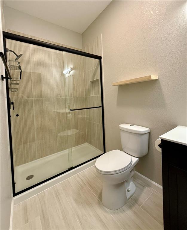 bathroom with toilet, vanity, a shower stall, and baseboards