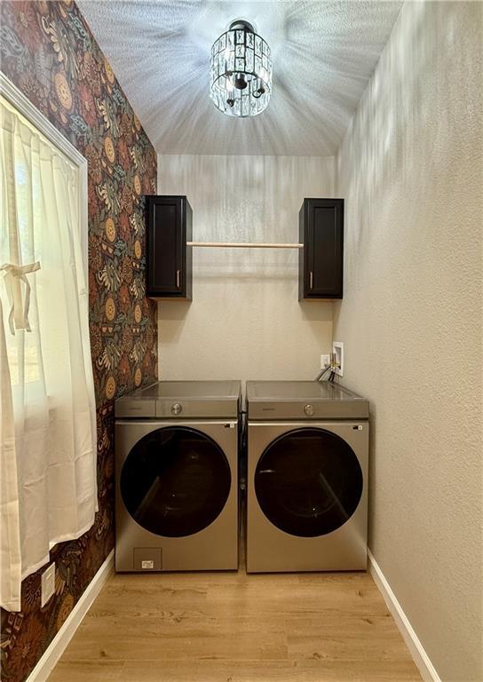 laundry room featuring washing machine and dryer, cabinet space, light wood finished floors, wallpapered walls, and baseboards